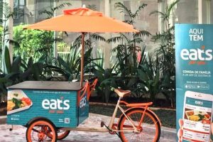 Carrinho de marmitas da startup de delivery, Eats For You, na rua. Ombrelone laranja e banner de divulgação da Eats4you.
