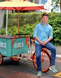 Fundador da Eats For You, Nelson Andreatta, sentado em um carrinho de marmitas da Eats For You.