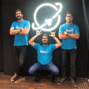 Os fundadores da AltruS, Cássio Fálcon e Bruno Aleixo, com Ivan Vemado, CTO da startup. Parede preta com logo do programa Planeta Startup.